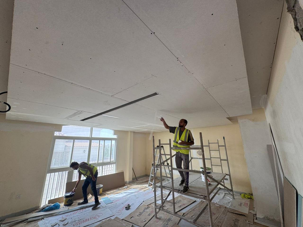 Gypsum board ceiling installation team on scaffold