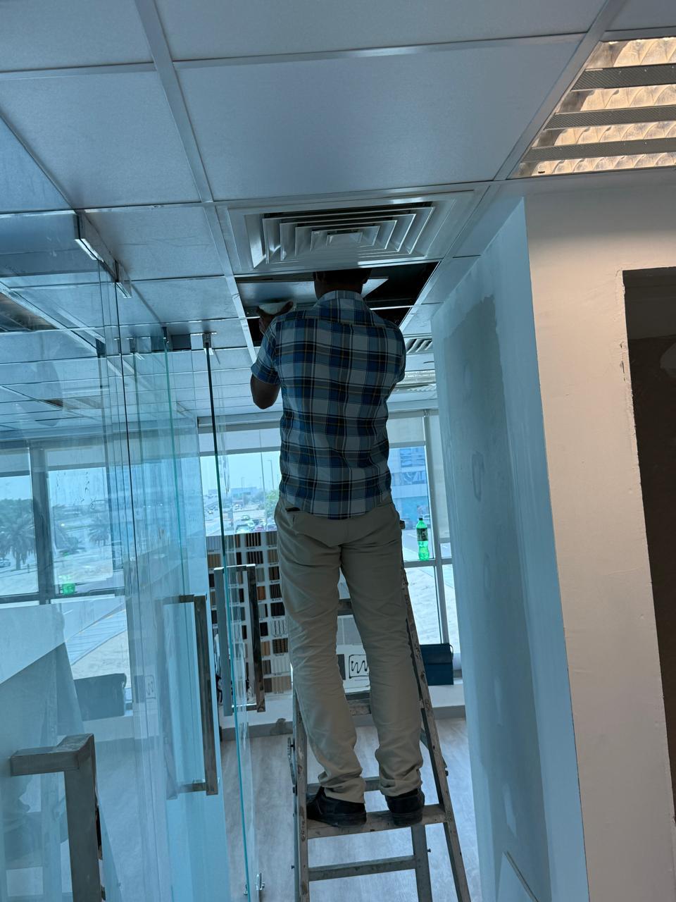 AC vent installation on ceiling by worker on ladder