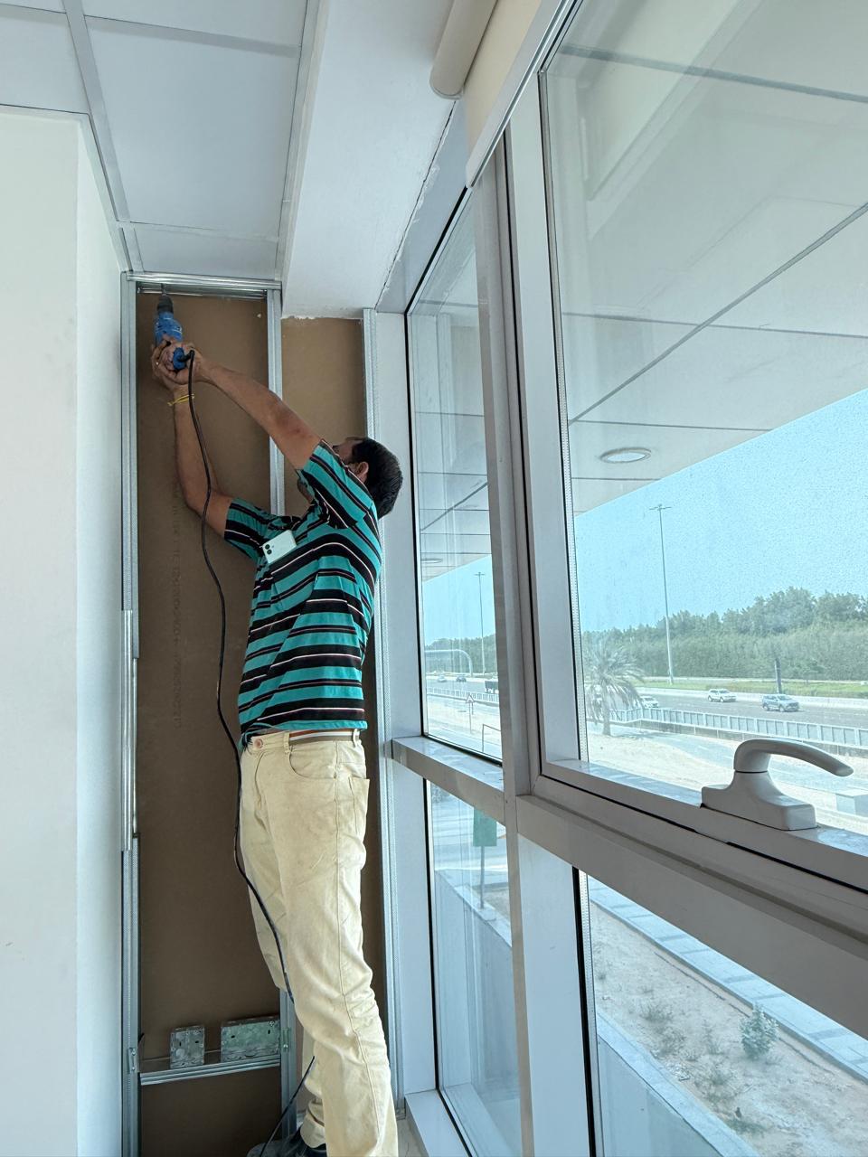 Worker drilling drywall partition near window