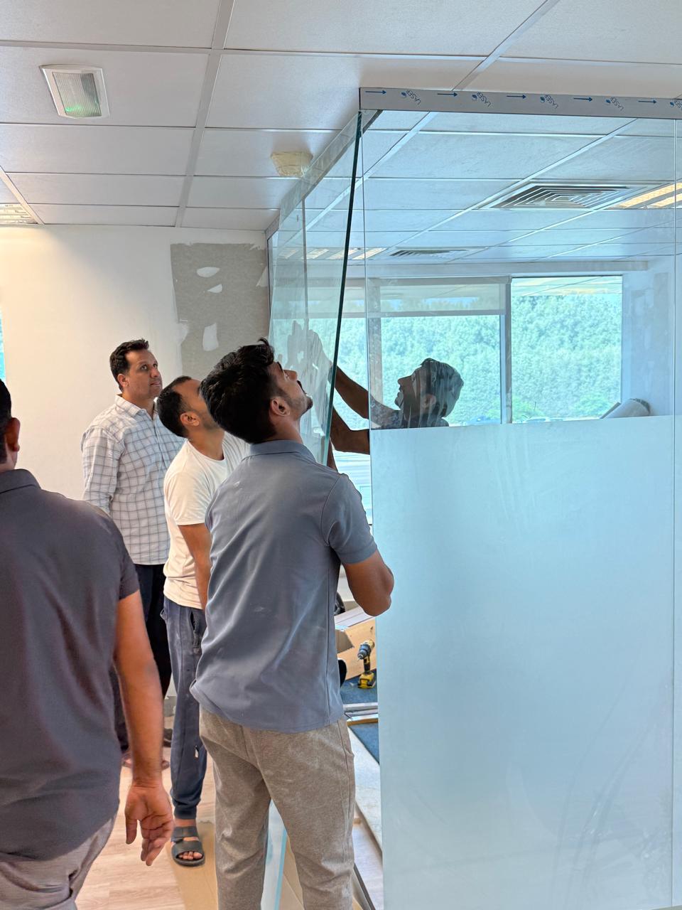 Workers fitting frosted glass partition in office
