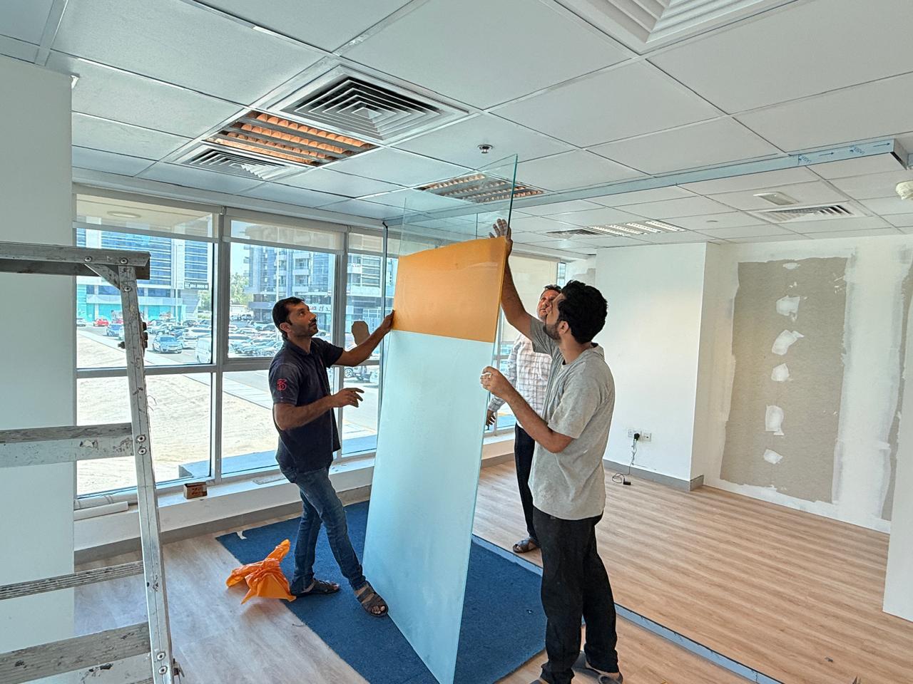 Team positioning glass partition panel in office