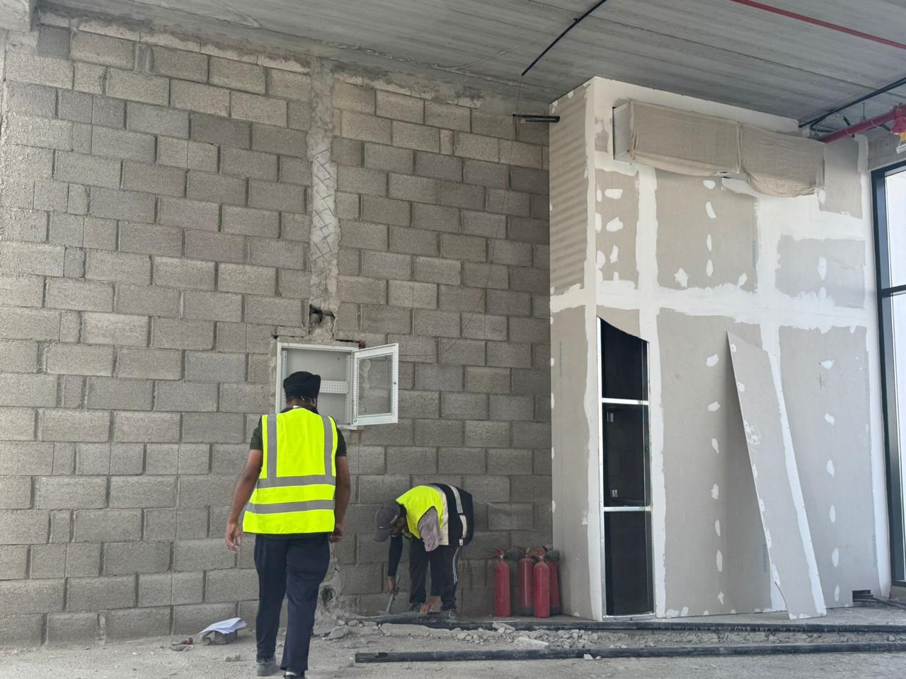 Workers inspecting blockwork wall and electrical panel box